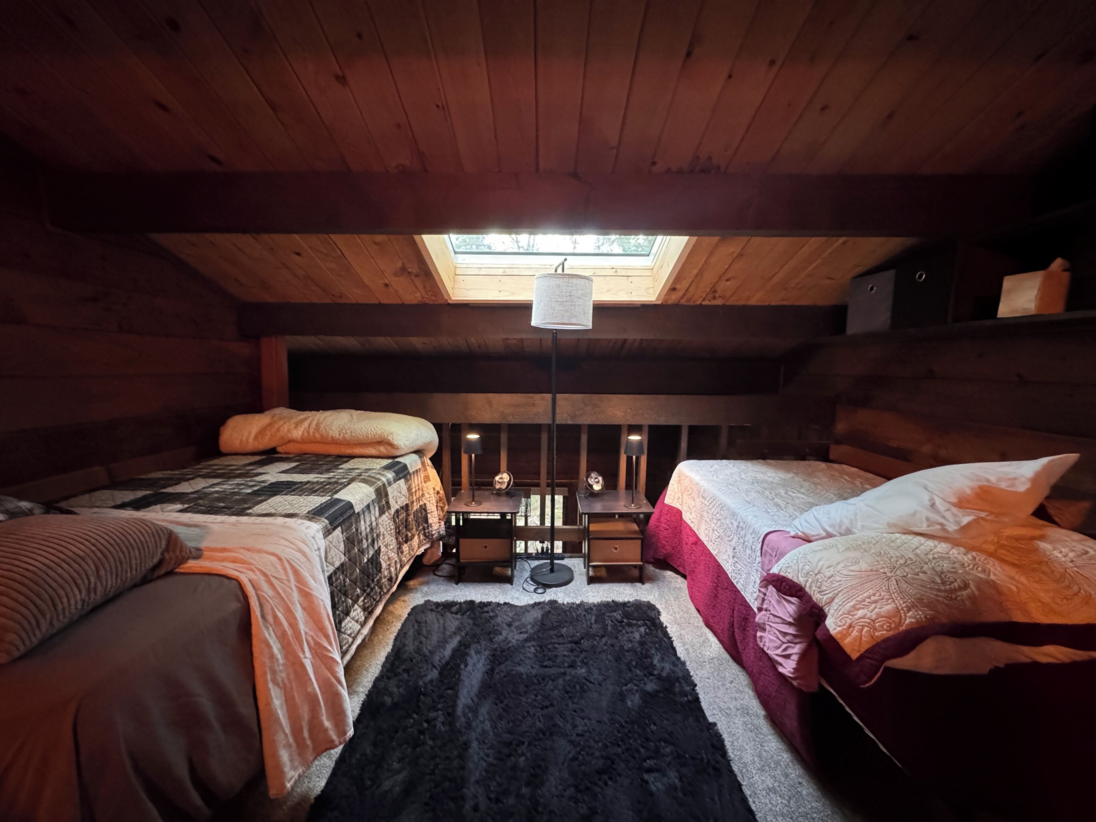 Una camera da letto mansardata accogliente con due letti, una finestra sul tetto e un piccolo tavolo con una lampada.