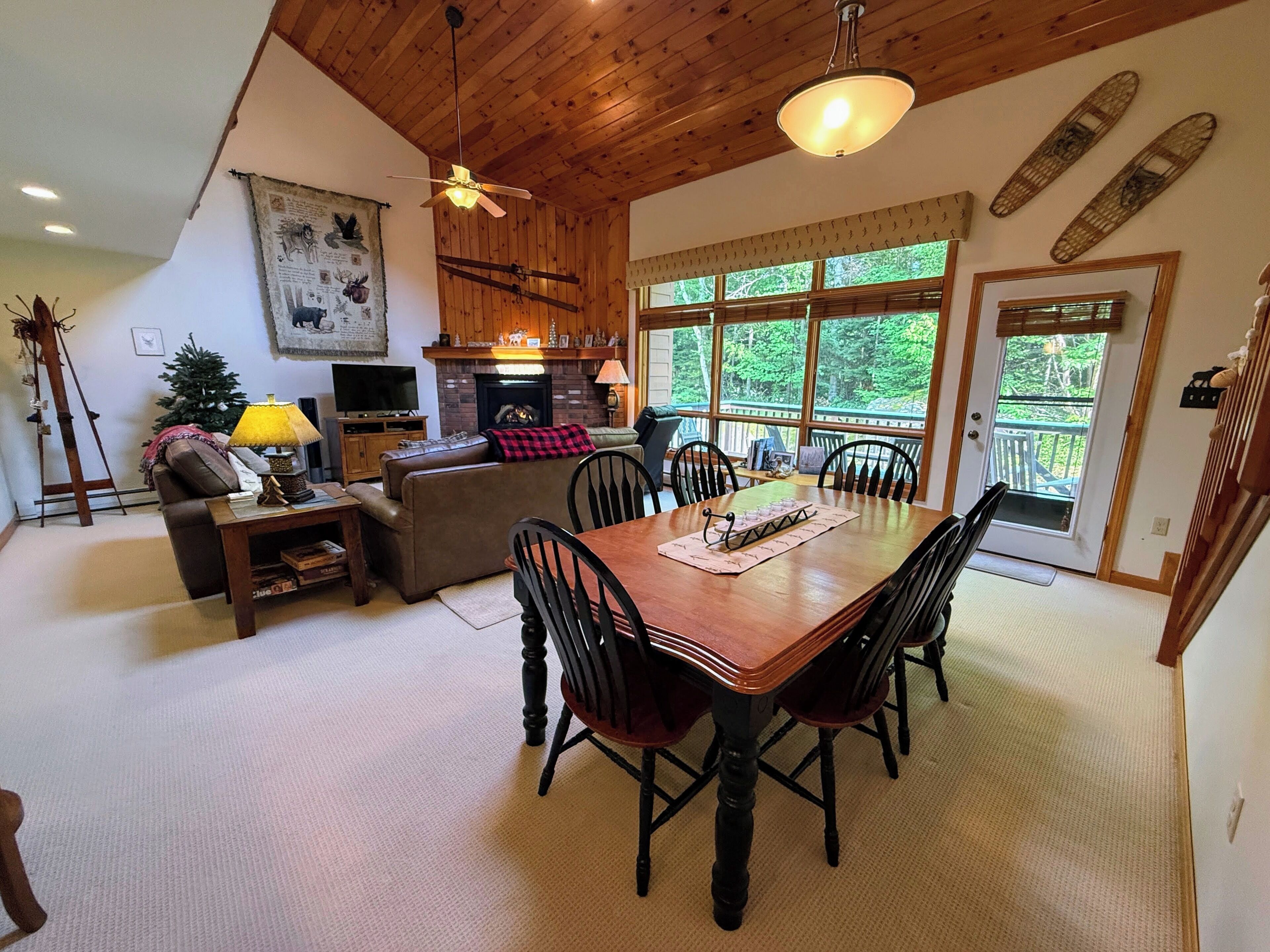 A cozy living room with a fireplace, a dining table with chairs, and a large window offering a view of the outdoors.