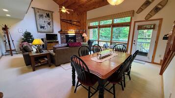 A cozy living room with a fireplace, a dining table with chairs, and a large window offering a view of the outdoors.