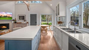 A modern kitchen with a large island, a built-in oven, and a dishwasher. There are multiple windows providing natural light and views of the outdoors. - Old Majors Family 4-Bed Retreat Southern Highlands (Braemar)