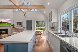 A modern kitchen with a large island, a built-in oven, and a dishwasher. There are multiple windows providing natural light and views of the outdoors. - Old Majors Family 4-Bed Retreat Southern Highlands (Braemar)