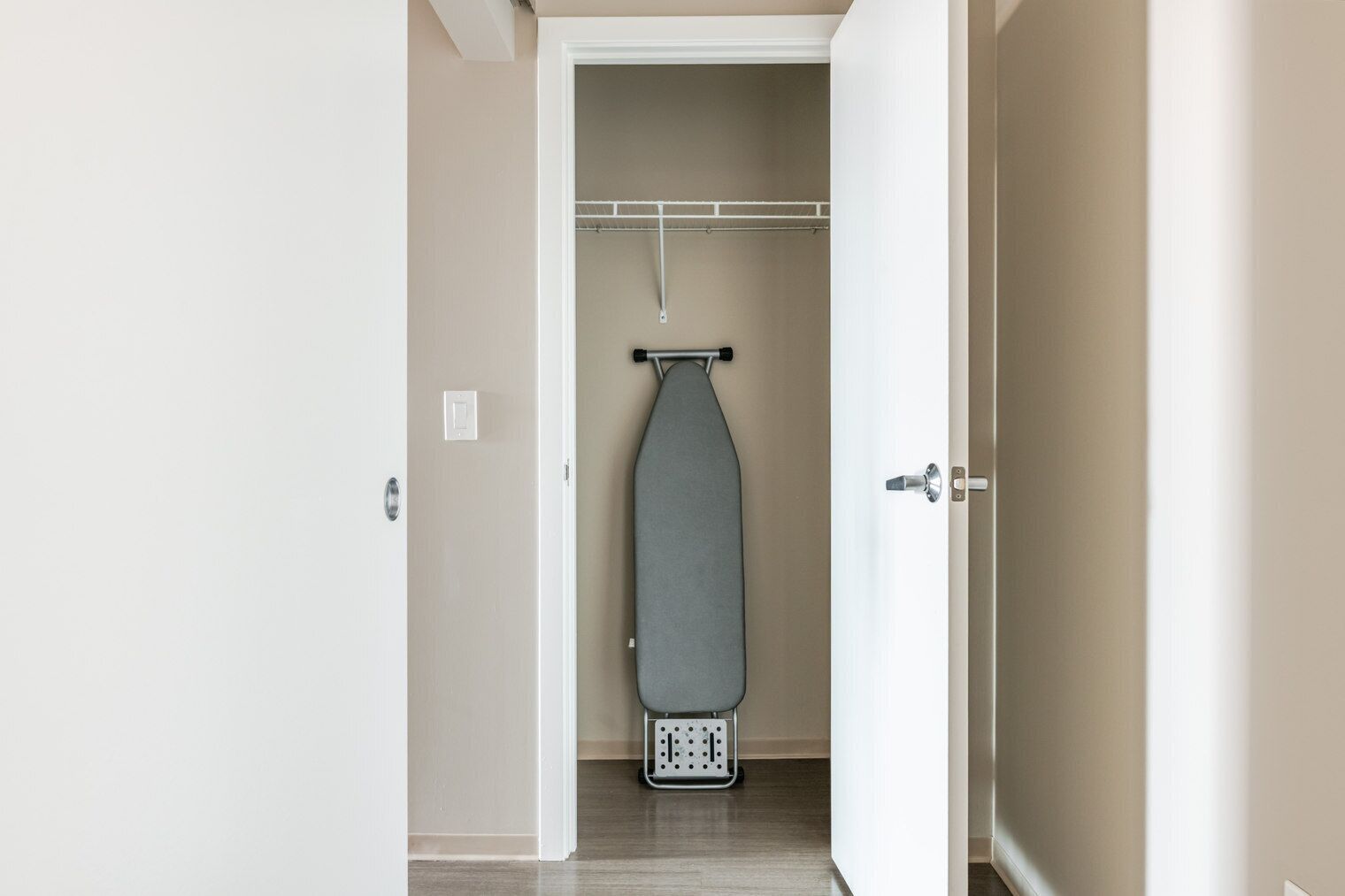 A hallway leading to a closet with a hanging rack and a shoe rack.