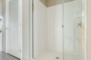 Une douche fermée par des parois de verre, avec des murs recouverts de carreaux blancs et une porte en métal dotée d’une poignée.