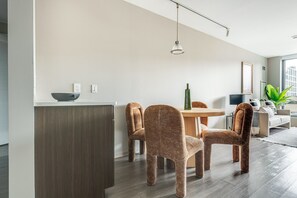 Ein modernes Wohnzimmer mit Essbereich, ausgestattet mit einem runden Tisch, vier Stühlen, einer Couch und einem großen Fenster.