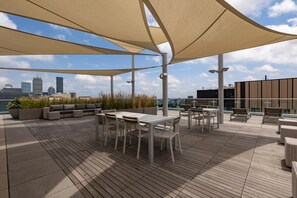 Une terrasse sur le toit offrant une vue panoramique sur la ville, avec une plateforme en bois, des sièges d’extérieur et de grandes structures en forme de parasol.