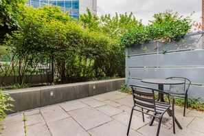 Une terrasse extérieure avec une table et des chaises, entourée de verdure et d’une clôture en métal.