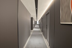 Ein moderner Hotelgang mit einem gemusterten Boden, eingelassener Beleuchtung und einem an der Wand befestigten Kunstwerk.