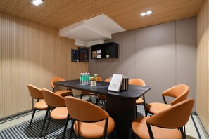 A conference room with a dark wooden table, orange chairs, and a white ceiling with recessed lighting.
