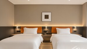 Una camera d'albergo con due letti, un comodino, una lampada a parete e un quadro incorniciato.