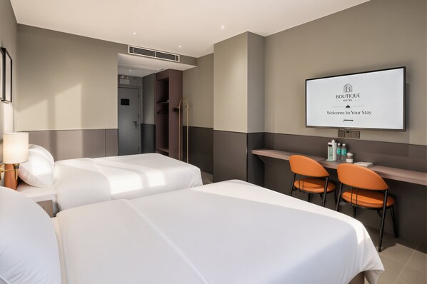 A hotel room with two beds, a desk with chairs, a television displaying a welcome message, and a shower area.