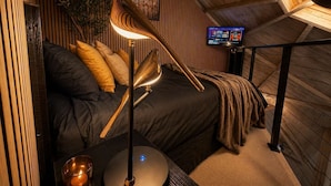 Et hyggeligt soveværelse med en seng, en moderne lampe, et lille bord og et fjernsyn.