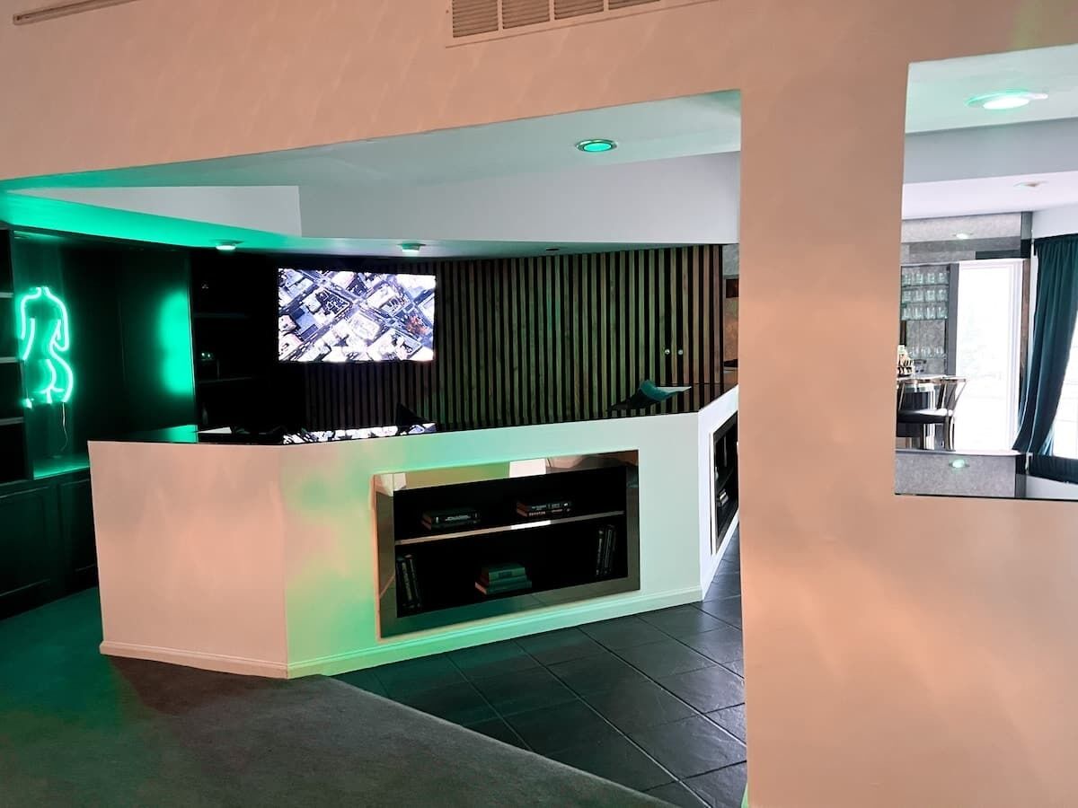 A modern reception area with a flat-screen TV, a white reception desk, and a green-lit neon sign.