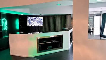 A modern reception area with a flat-screen TV, a white reception desk, and a green-lit neon sign.