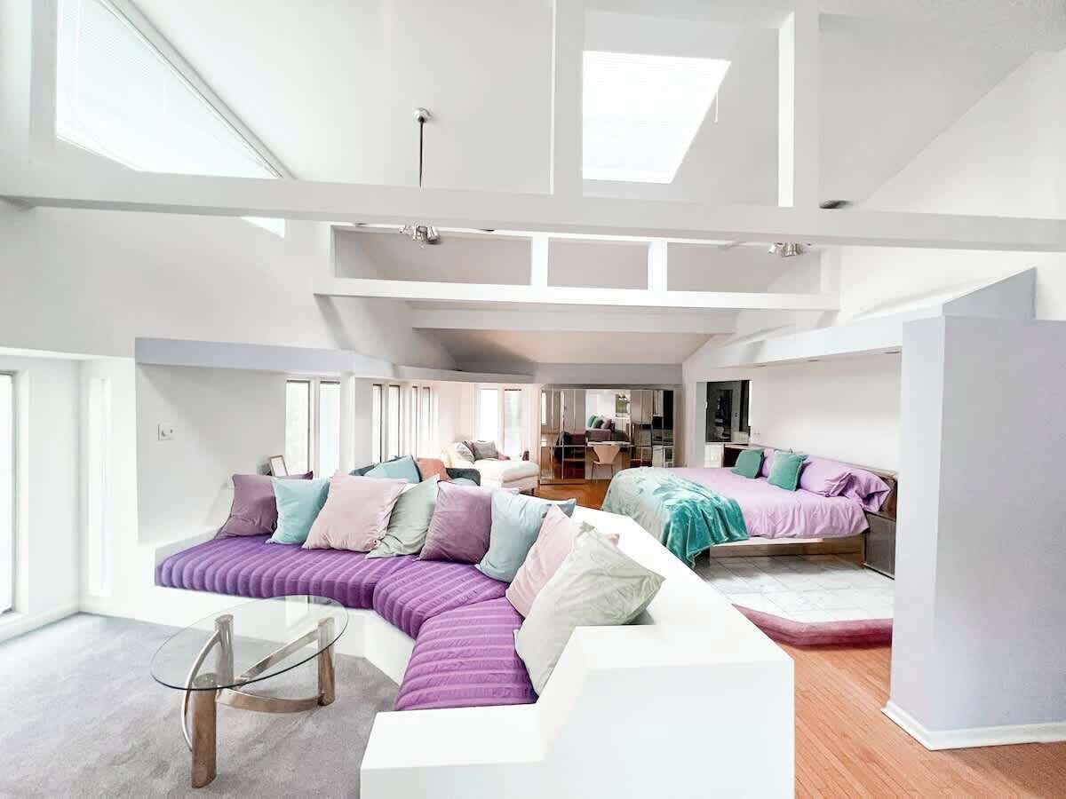 Un intérieur moderne avec un grand canapé d’angle, une table basse en verre et un lit doté d’une tête de lit.