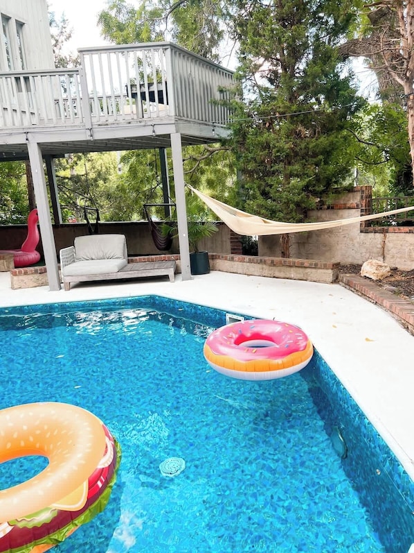 A swimming pool with two inflatable rings, a hammock, and a white outdoor seating area.