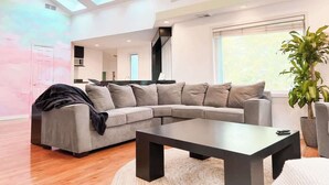 A modern living room with a sectional sofa, a coffee table, and a large window with natural light. - Luxury  Villa w/ Pool, Max Amenities (Kansas City)