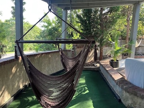 A hammock suspended from a metal frame, a brick wall, and a green artificial turf area.