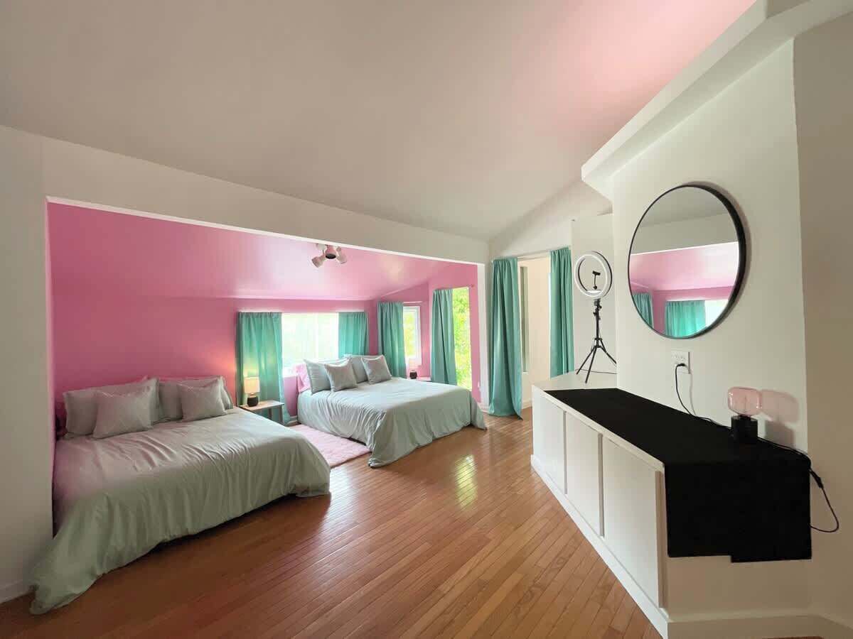 A bedroom with two beds, a desk, a mirror, and a ceiling fan.