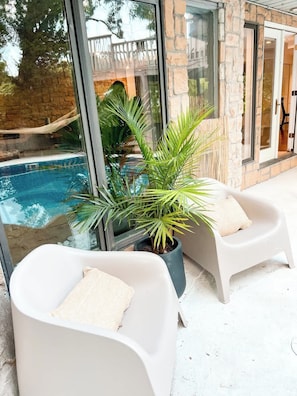 Zona junto a la piscina con dos sillones blancos y una palmera en maceta.