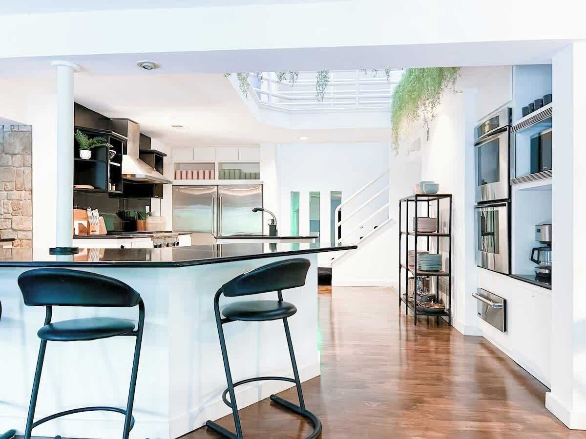A modern kitchen with a central island, bar stools, and a staircase leading to an upper level.