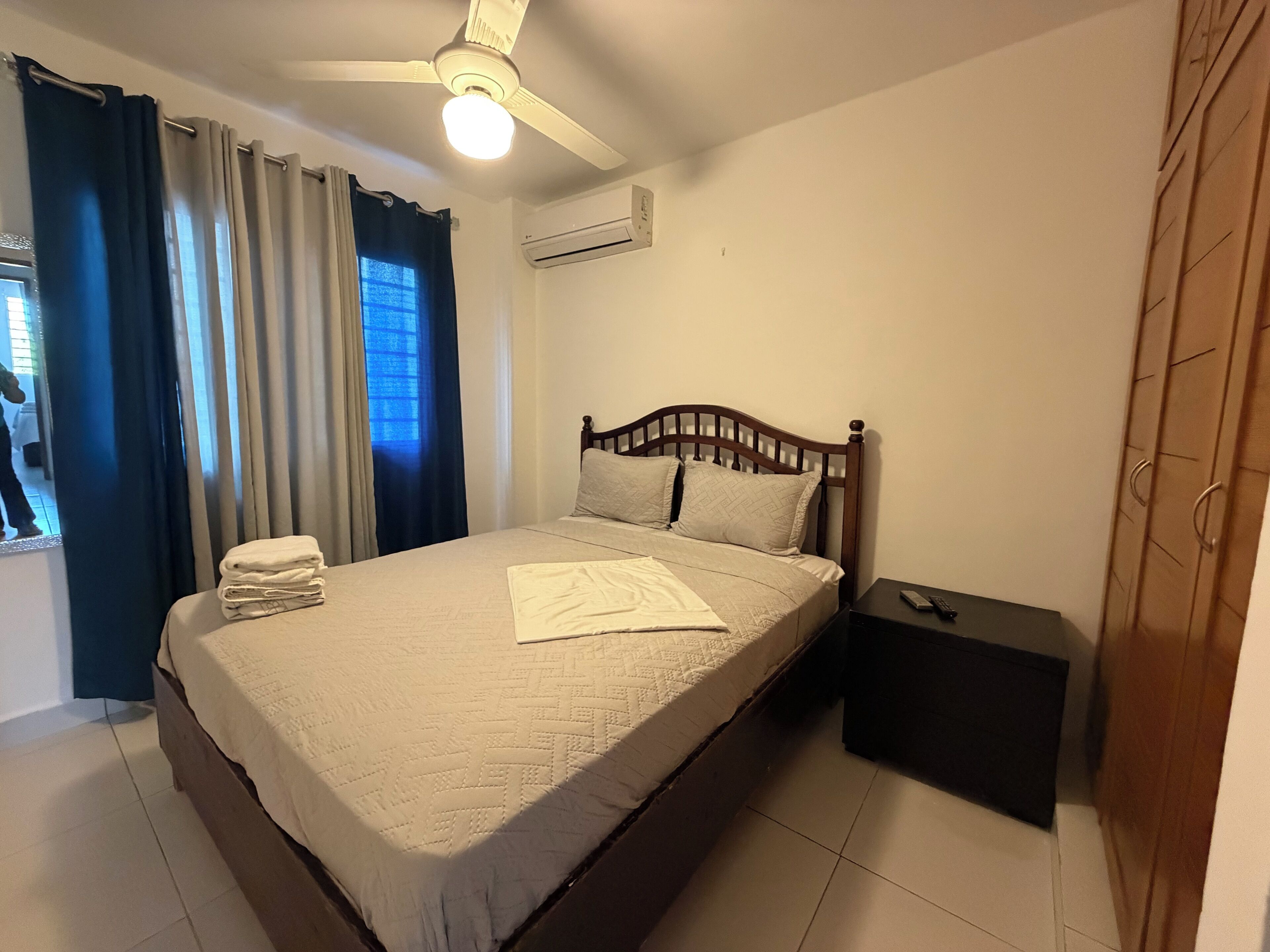 Ein Schlafzimmer mit Bett, Nachttisch, Kleiderschrank und Deckenventilator.