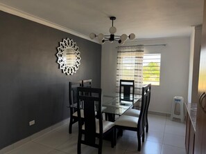 A dining area with a glass table and chairs, a decorative wall piece, and a window with curtains. - Palma real  (Puñal)