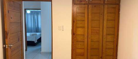 Un dormitorio con un armario de madera, una cama con edredón blanco y un baño visible a través de una puerta abierta.