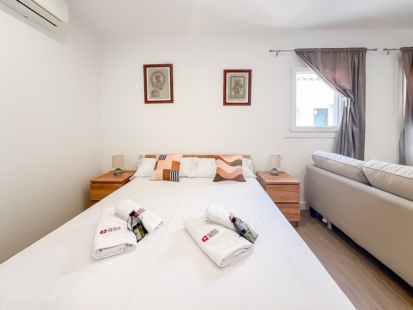 Una habitación de hotel con una cama, dos mesitas de noche, un sofá y dos cuadros en la pared.