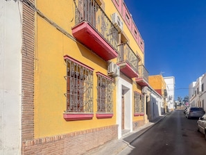 A street view with yellow buildings, red balconies, and barred windows. - GuestReady - Casa Espelete 1B (El Puerto de Santa María)