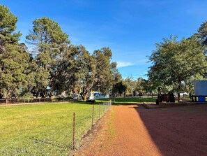 A fenced outdoor area with a gravel path, green grass, and trees. - Tiny Home in the Hills by Tiny Away (Forrestfield)