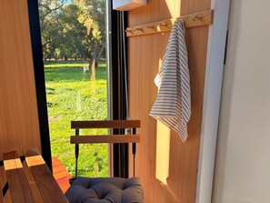 A room with a wooden bench, a cushioned seat, and a window with a view of a green park. - Tiny Home in the Hills by Tiny Away (Forrestfield)