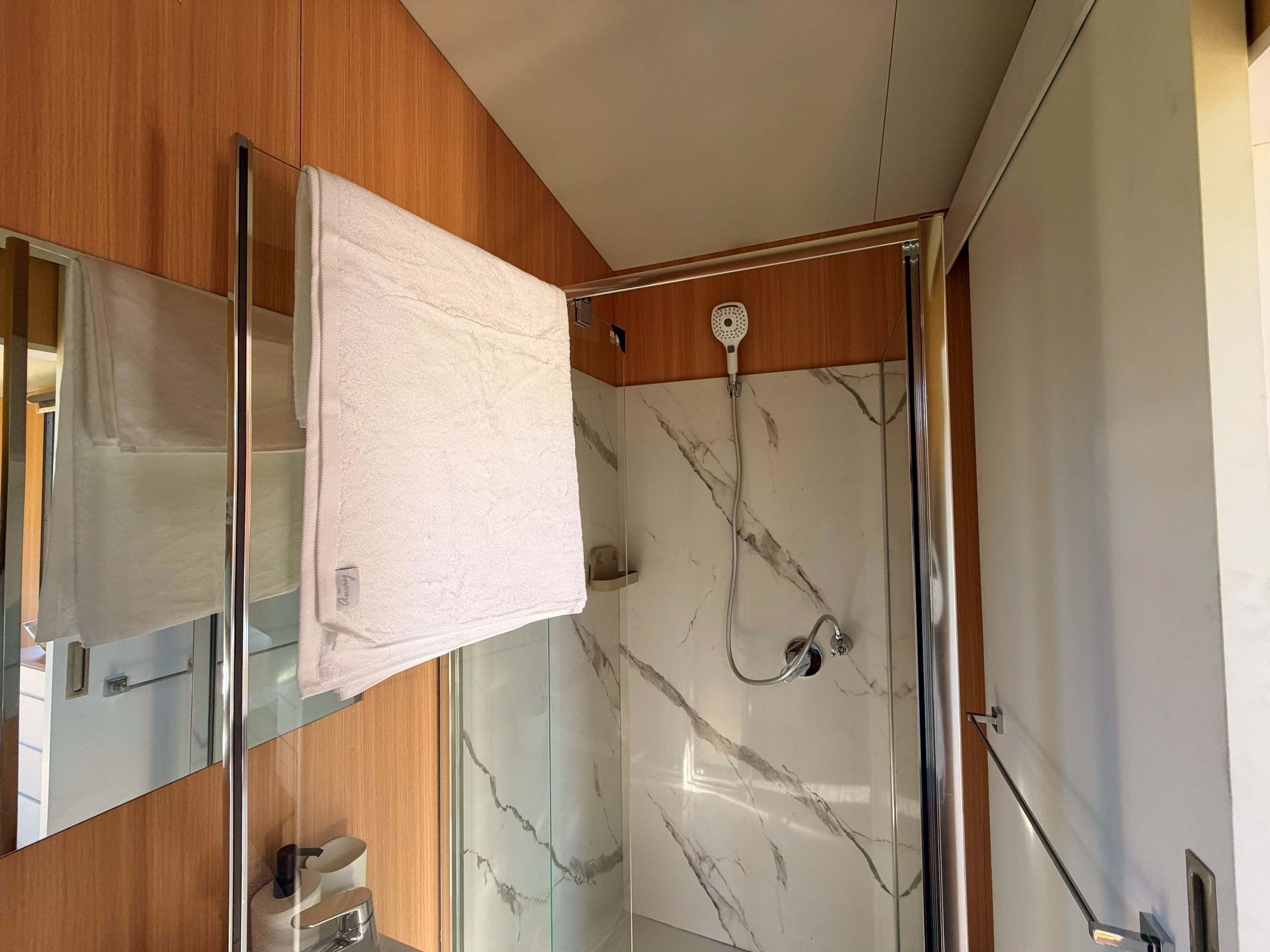 A modern bathroom with a glass shower enclosure, a marble backsplash, and a wooden vanity.