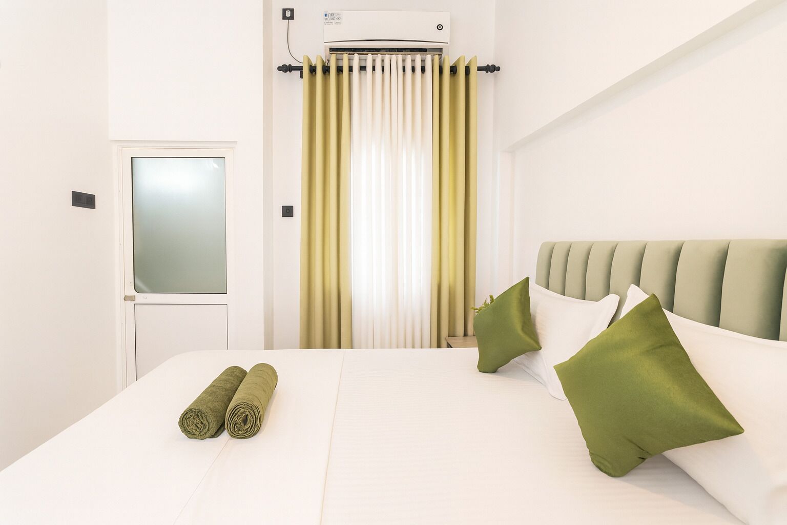 A hotel room with a bed, a window with curtains, a radiator, and a door.