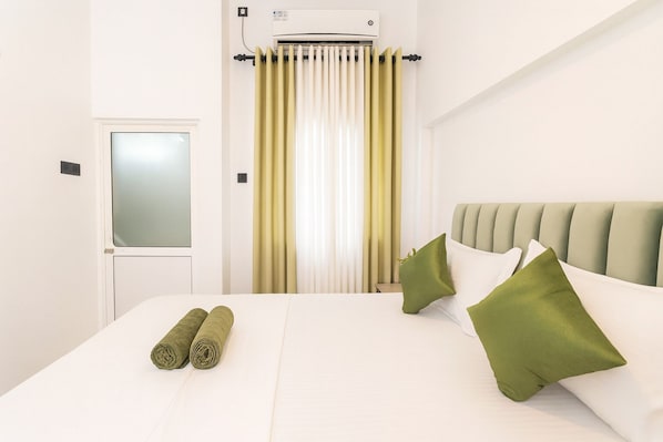 Una habitación de hotel con cama, ventana con cortinas, radiador y puerta.