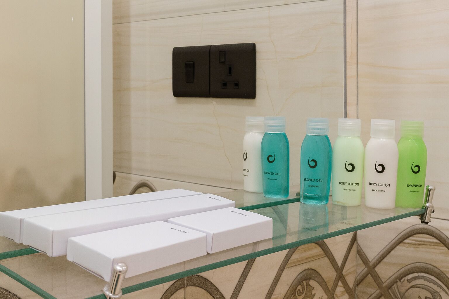 Casa de banho com uma prateleira de vidro com produtos de higiene, uma pia branca e uma tomada elétrica preta na parede.