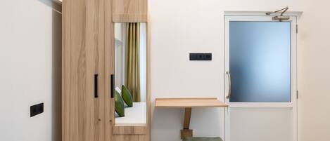 Ein Zimmer mit Holzschrank, kleinem Tisch, Bank, Tür mit Milchglas und Lichtschalter an der Wand.
