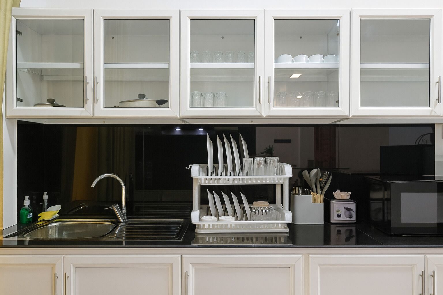 Una cocina con armarios blancos, un lavamanos y un escurreplatos.