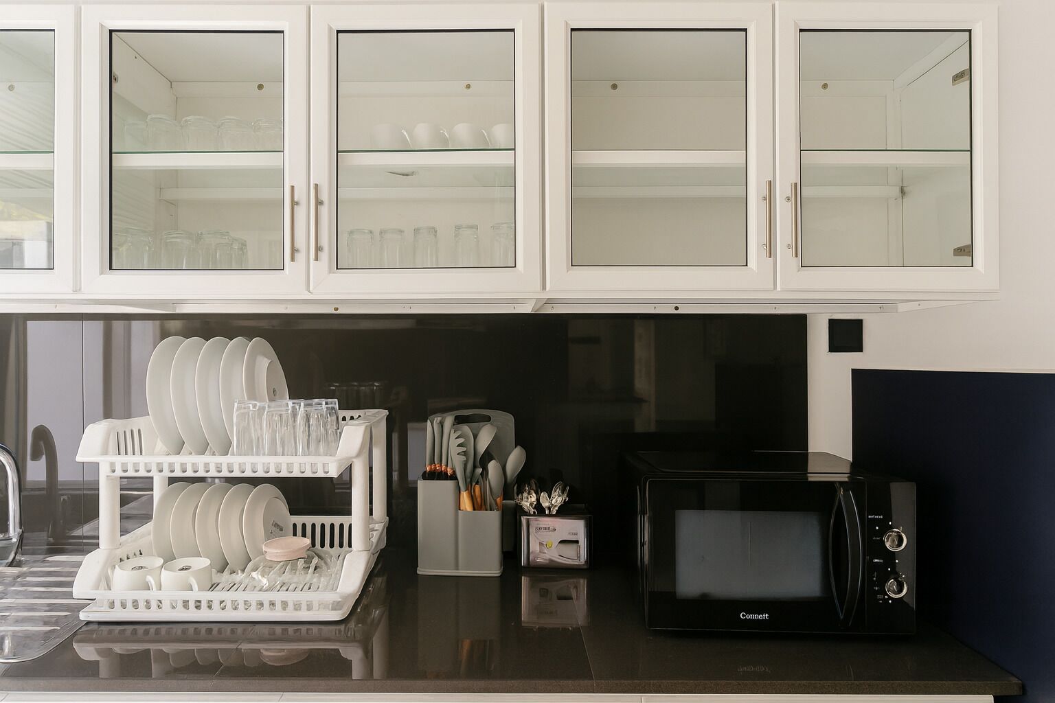 A kitchen with white cabinets, a dish rack, a microwave, and a coffee maker.