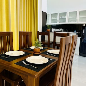 Una mesa de comedor con seis sillas, una planta en maceta y una cocina al fondo.