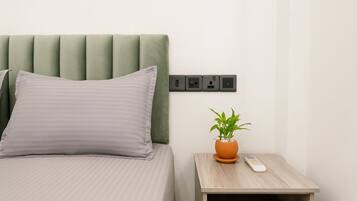 A bed with a green headboard, a grey pillow, a bedside table with a potted plant, and a remote control.