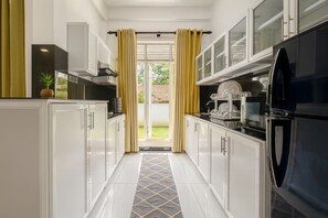 A kitchen with white cabinets, a black refrigerator, and a tiled floor. - Skyport Villa Katunayaka (Katunayake)