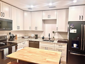 A kitchen with white cabinets, a wooden table, a black refrigerator, and a microwave. - Peaceful St. Pete 2BR Home with Tropical Garden (St. Petersburg)