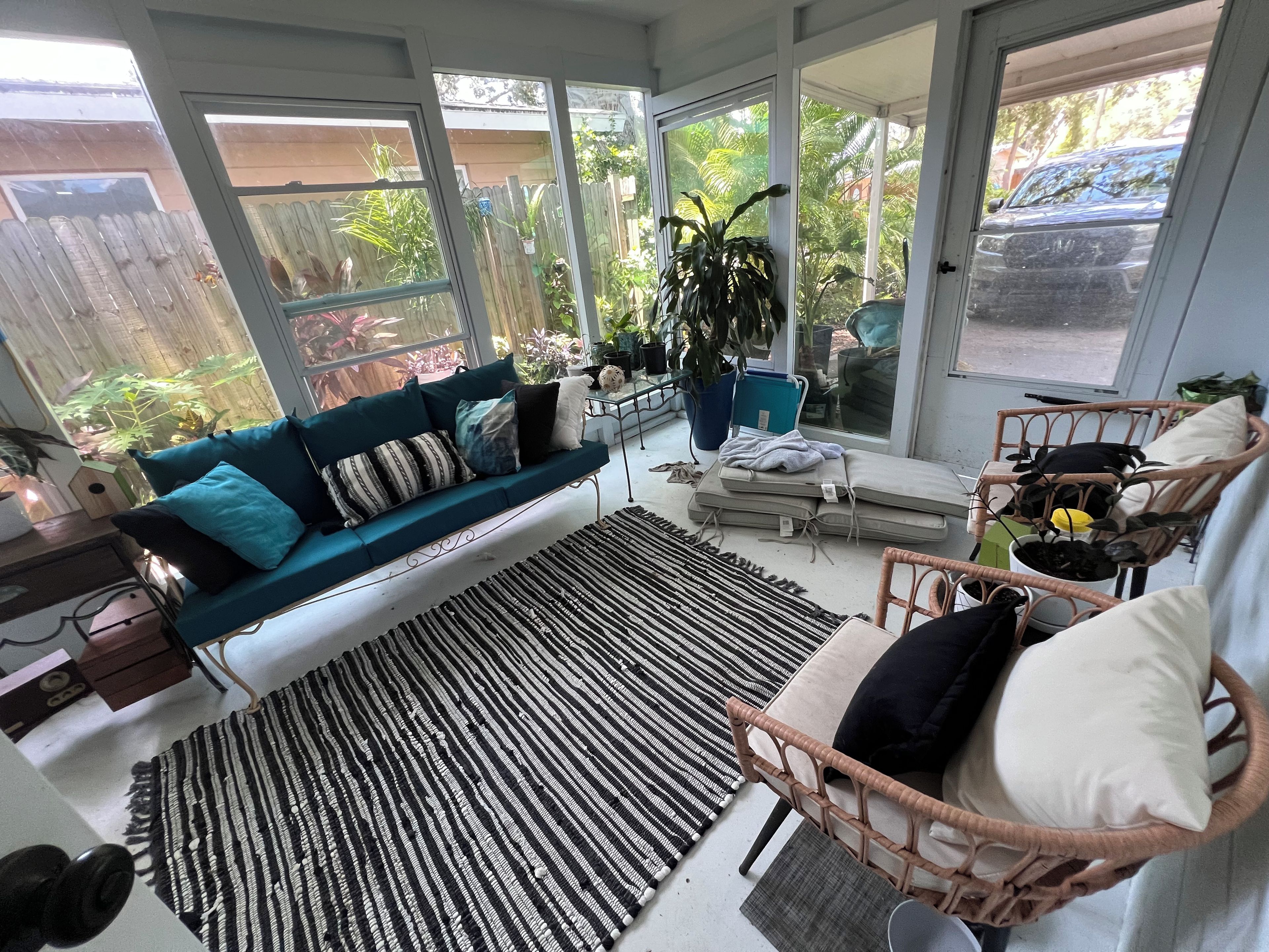 A sunlit room with a blue sofa, a wicker chair, and a large window overlooking a garden.