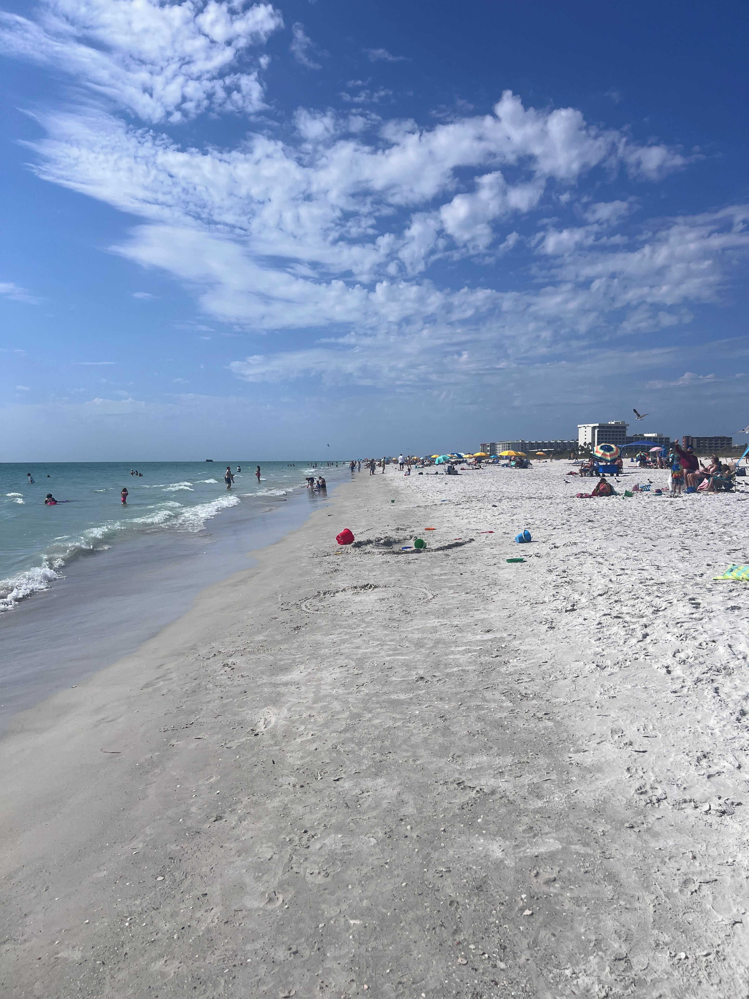 A beach with people swimming and walking, umbrellas, and beach chairs.