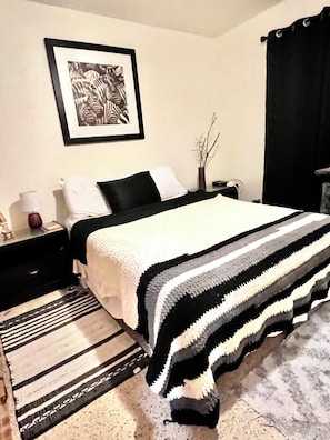 A neatly arranged bedroom with a bed, bedside table, lamp, and a framed picture on the wall. - Peaceful St. Pete 2BR Home with Tropical Garden (St. Petersburg)