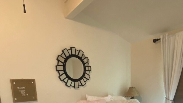 Quarto com cama, mesa de cabeceira, espelho fixado na parede e placa de boas-vindas.