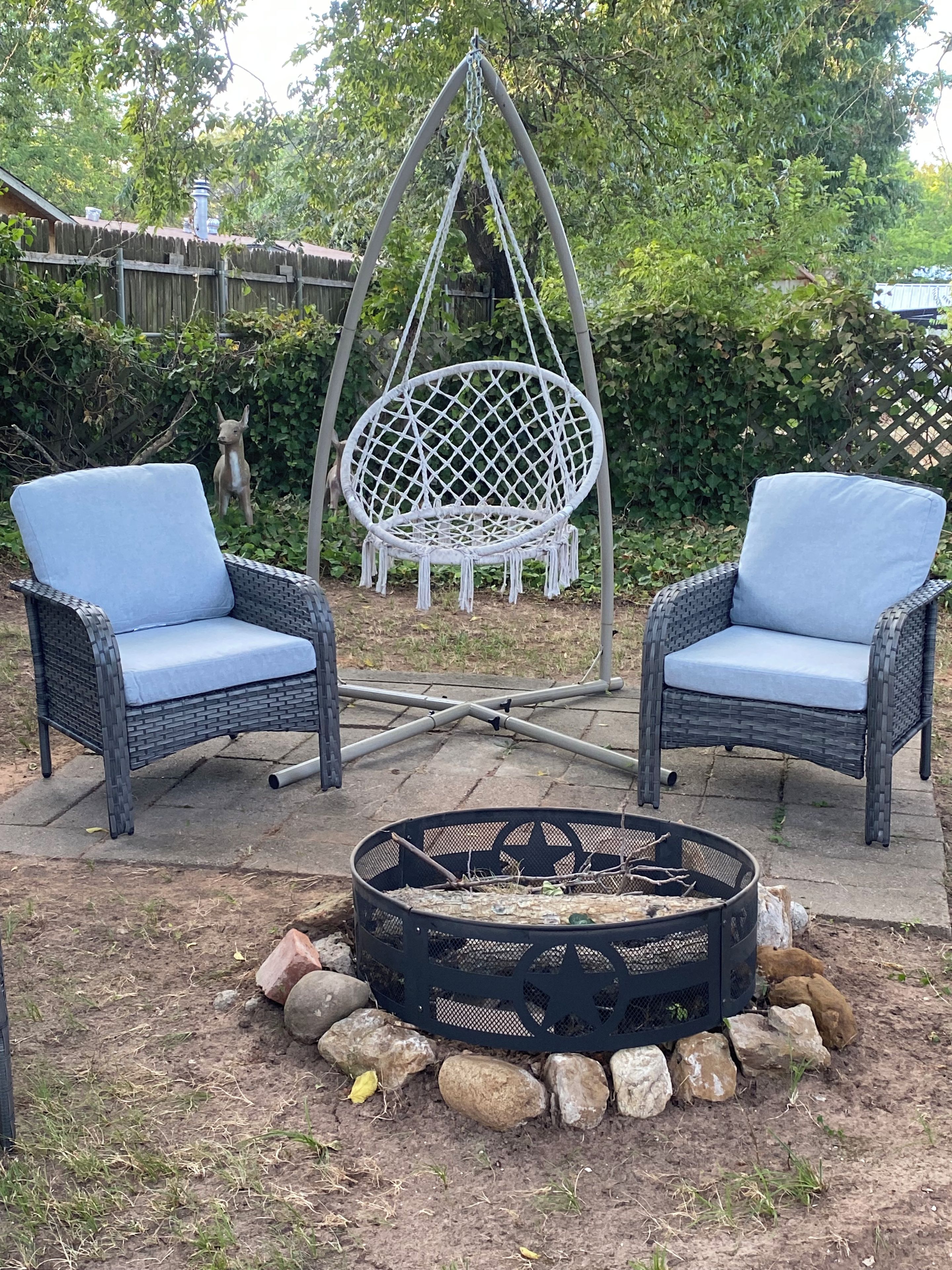 Two wicker chairs with blue cushions, a hanging swing chair, and a fire pit with rocks.