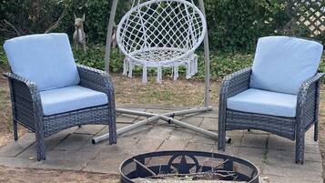 Two wicker chairs with blue cushions, a hanging swing chair, and a fire pit with rocks.
