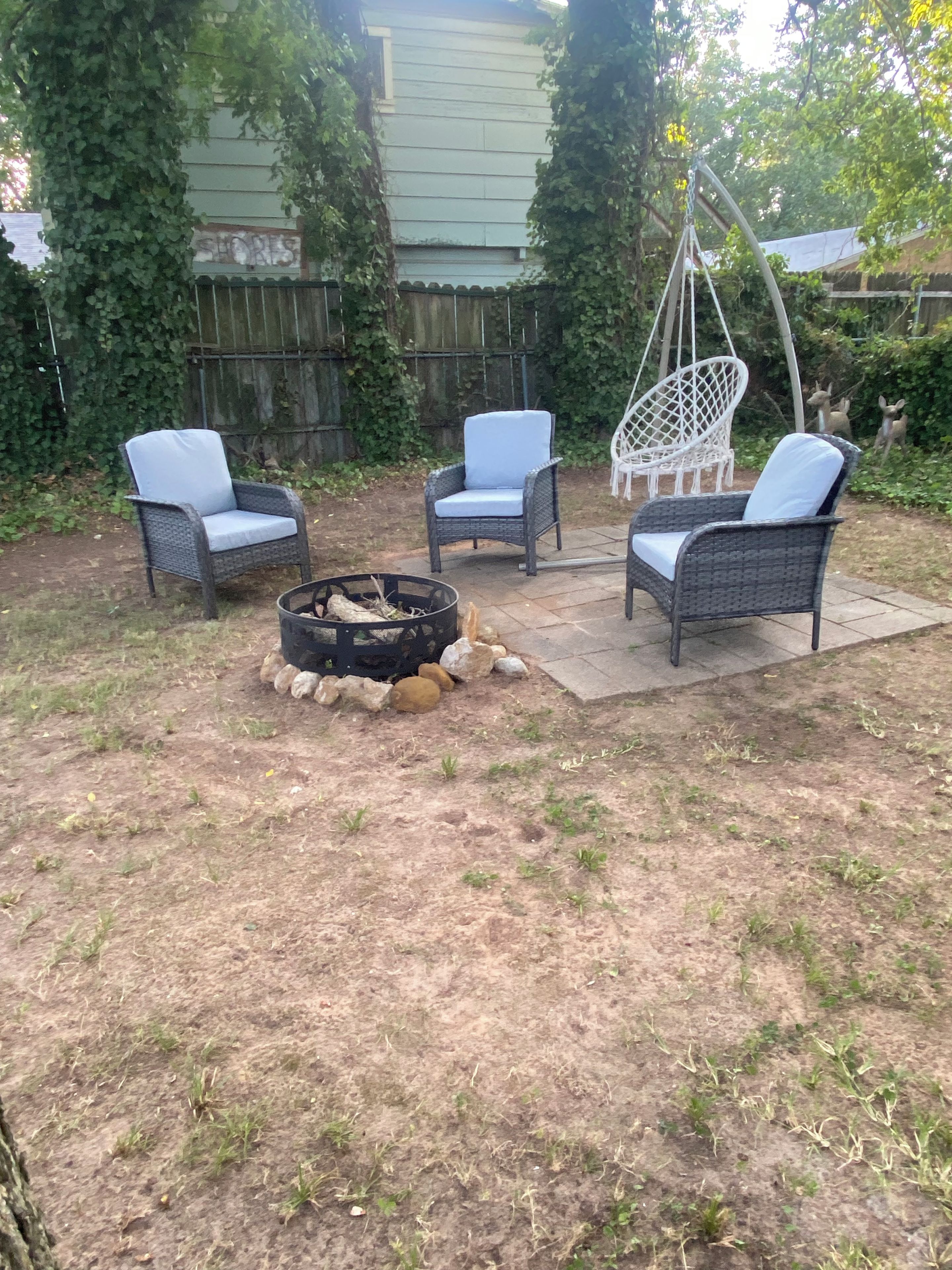 Un jardin avec un foyer, trois fauteuils en osier et une chaise suspendue.