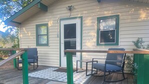 Um deck de madeira com guarda-corpo, uma porta e duas janelas com molduras verdes.